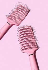 Brosse à cheveux rose avec une forme de paddle large, des poils en plastique flexibles et un manche lisse accentué par une bague métallique argentée.