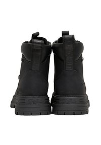 Bottes noires à la cheville avec une texture mate, talon renforcé et semelle crantée prononcée. Dotées d'une languette de tirage avec logo et d'un rembourrage à la cheville.