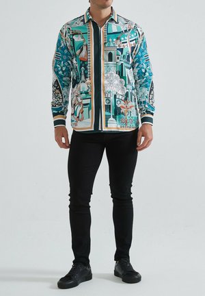 Chemise à boutons avec des motifs complexes teal et blancs, présentant des designs floraux et architecturaux. Manches et col noirs contrastants.