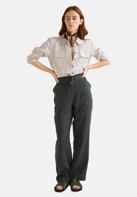 Chemise en lin gris clair avec un devant à boutons et des poches sur la poitrine, associée à un pantalon ample vert foncé avec une taille à cordon.