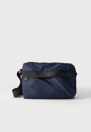 Sac bandoulière rectangulaire bleu marine, avec une bandoulière noire réglable, une fermeture zippée et le logo Björn Borg, présenté sur un fond uni.