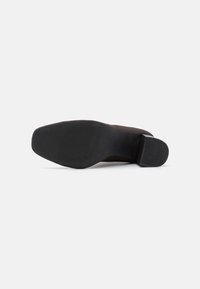 Scarpa in suede marrone con tacco basso. La suola è in gomma nera con un motivo di grip testurizzato. Il design presenta una forma elegante e affusolata.