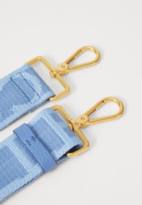 Cinturino in tessuto azzurro chiaro con clip in metallo dorato. Presenta un accento in pelle liscia con dettagli di cucitura. Il design enfatizza funzionalità e stile.
