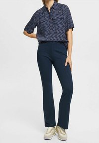 Pantaloni fitted blu navy con una finitura testurizzata, abbinati a una camicia a maniche corte a fantasia con due tasche sul petto e un colletto.
