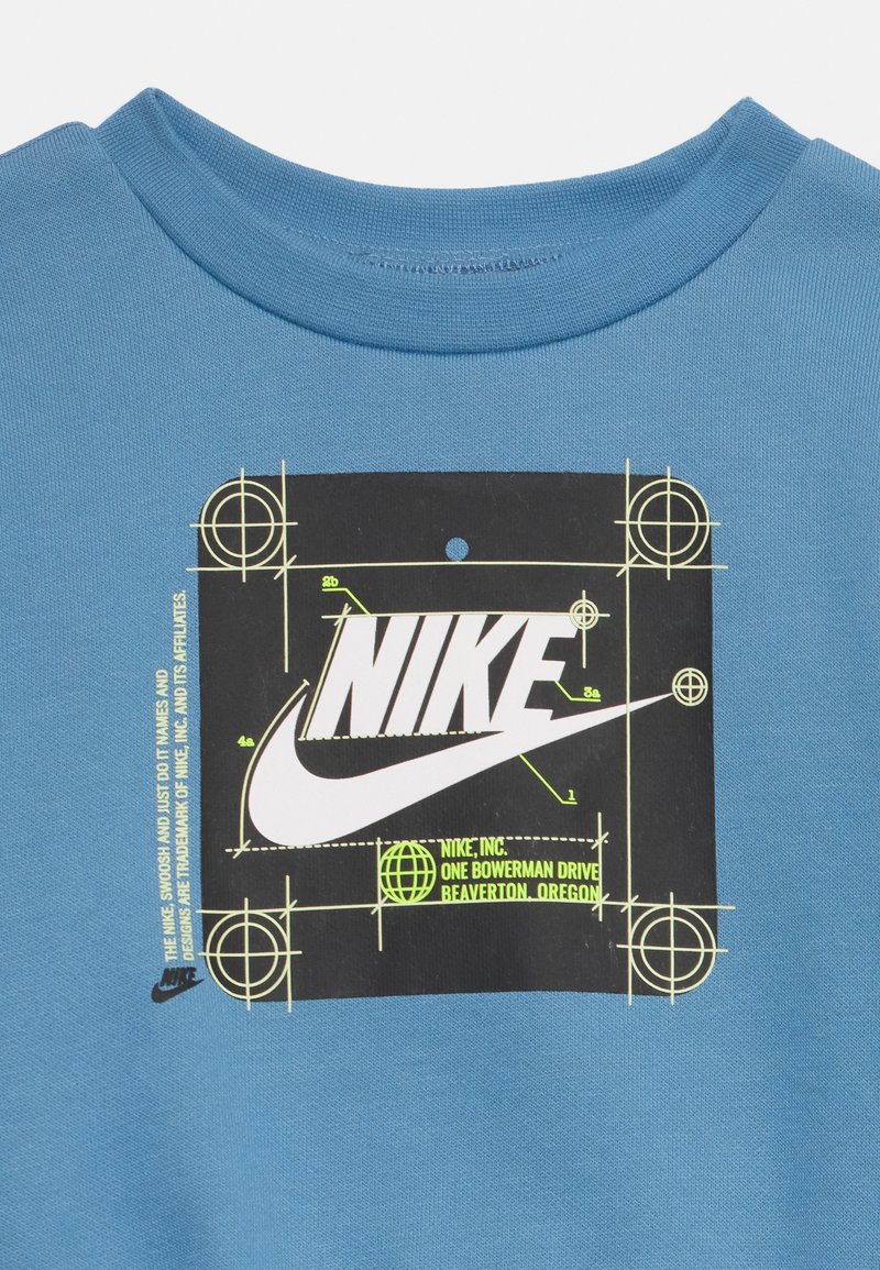 Blaues Baumwoll-T-Shirt mit einem zentralen schwarzen Grafiken, grünen geometrischen Markierungen und einem weißen Nike-Logo, runder Ausschnitt und kurzen Ärmeln.