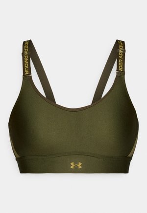 Zaļa sporta krūšturis ar regulējamiem siksnām, kurā ir "UNDER ARMOUR" zīmols. Izgatavots no gludas, elastīgas vielas ar bezšuvju dizainu.