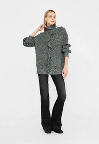 Chunky grey sweater with a high collar and a ruffled front, paired with flared black jeans and black shoes. Smooth texture and oversized fit.