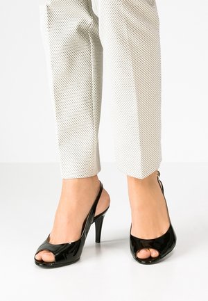 Schwarze Slingback-Pumps mit hohen Absätzen und offenen Zehen, getragen mit knielangen Hose im weißen Polka-Dot-Muster, die ein modisches Outfit präsentieren.