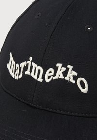 Casquette noire avec logo "Marimekko" brodé en blanc. Matière en toile avec une coupe structurée, coutures visibles et œillets de ventilation.