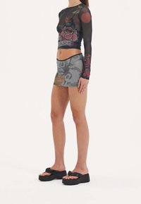 Langärmliges, transparentes Oberteil mit floralen Druck in dunklen Farben, kombiniert mit einem taillierten, gemusterten Minirock und klobigen schwarzen Plateau-Sandalen.