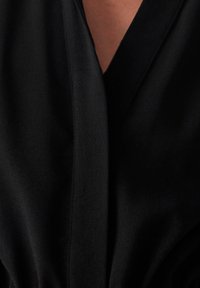 Lähikuva henkilöstä, joka on pukeutunut mustaan vaatteeseen, jossa on syvä V-pääntie, joka paljastaa osan ylärintakehästä.