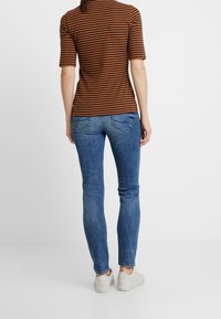 Top de manga corta a rayas marrones combinado con jeans ajustados azules y zapatillas blancas, mostrando un diseño casual y contemporáneo.