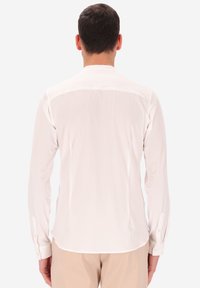 Camicia bianca a maniche lunghe con una texture liscia, colletto classico, polsini con bottoni e orlo curvo, vista da dietro.