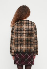 Καρό μάλλινο σακάκι σε καφέ, μαύρο και μπεζ, με κουτί σχήμα και στρογγυλή λαιμόκοψη. Συνδυάζεται με φούστα σε σχήμα houndstooth.