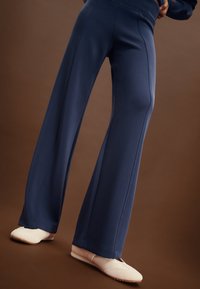 Navyblaue Hosen mit weitem Bein aus weichem Stoff, mit Nahtdetails und einem lockeren Sitz, kombiniert mit hellen flachen Schuhen.