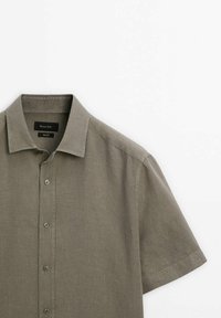 Korte mouwen, licht olijfgroen knoopshirt van linnen stof. Heeft een klassieke kraag en een rechte snit, met zes knopen aan de voorkant.