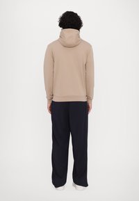 Hanorac bej cu glugă, cu o croială lejeră, dintr-o țesătură texturată, cu manșete elastice, asortat cu pantaloni largi de un bleumarin închis și încălțăminte albă.