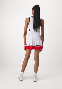 White athletic dress with a flared red skirt and black accents, featuring a round neckline and sleeveless design. Back view.