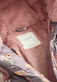 Rosa Kunstpelz-Futter mit einer glatten, grauen Außenseite, die mit Blumenmustern verziert ist. Das Etikett trägt die Marke "NEXT".