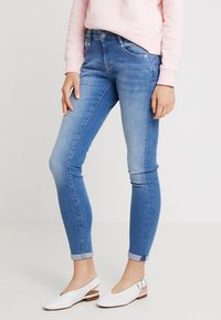 Modré džíny s úzkým střihem, vybledlým designem a ohrnutými manžetami. V kombinaci s bílými nazouvanými botami a světle růžovou mikinou.