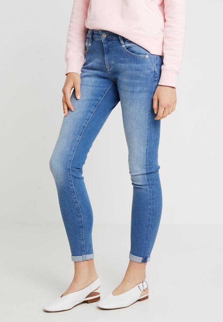 Modré džíny s úzkým střihem, vybledlým designem a ohrnutými manžetami. V kombinaci s bílými nazouvanými botami a světle růžovou mikinou.