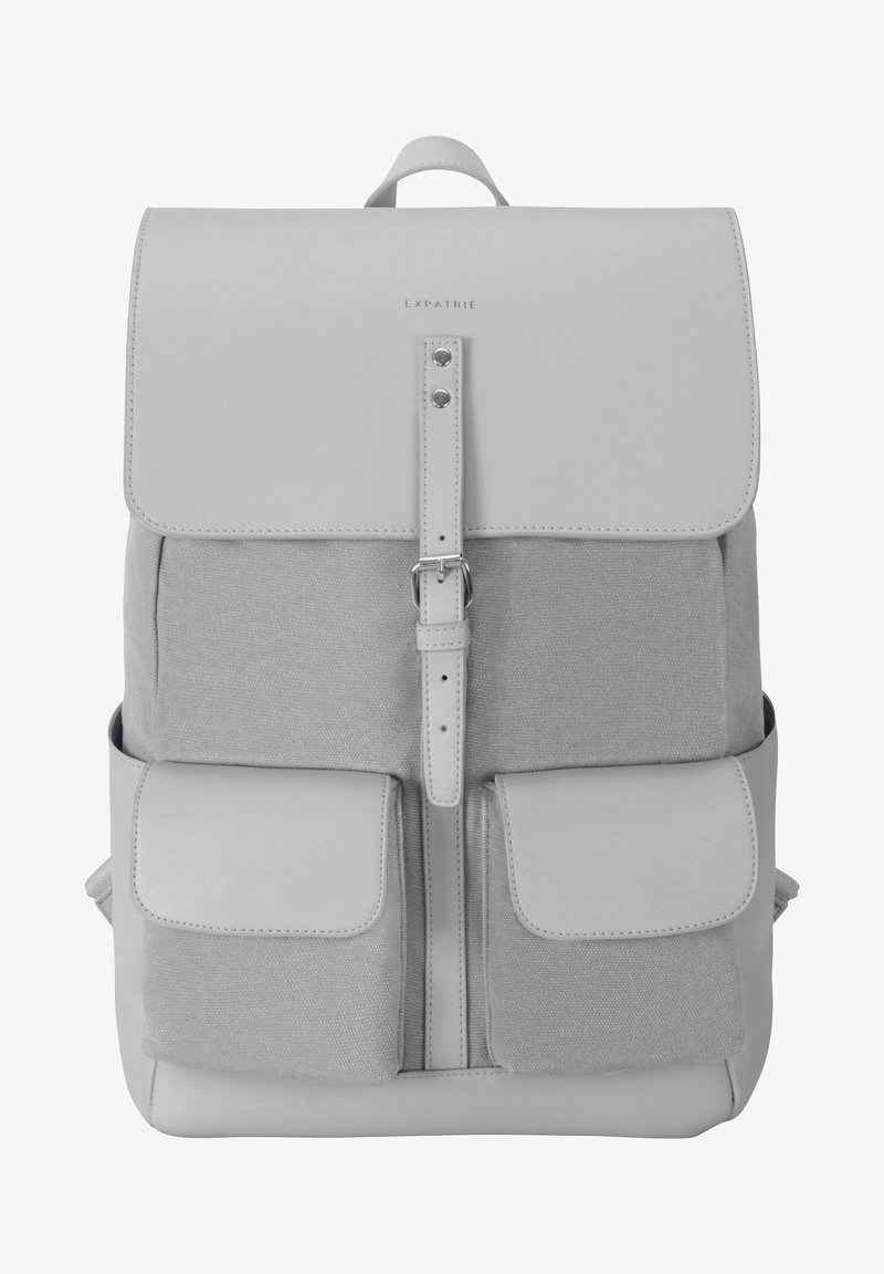 Sac à dos gris en cuir et toile, avec un rabat de fermeture, deux poches avant et un design de sangle simple.