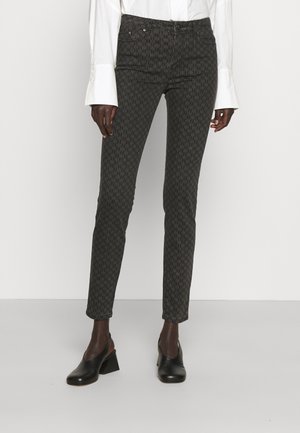 Donkergrijze slim-fit broek met een subtiel geweven patroon, gecombineerd met zwarte schoenen met hakken en een wit overhemd met lange mouwen en wijde manchetten.