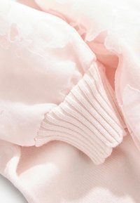 Ljust rosa tyg med mjuk blommönstring; inkluderar ribbade manschetter för en figurnära design. Materialet ser slätt och lätt ut.