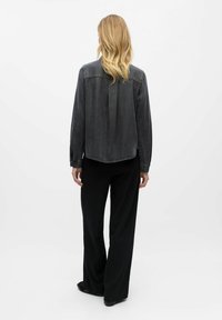 Chemise en denim gris foncé à manches longues, coupe décontractée, avec un pli dans le dos, assortie à un pantalon large à rayures noires.