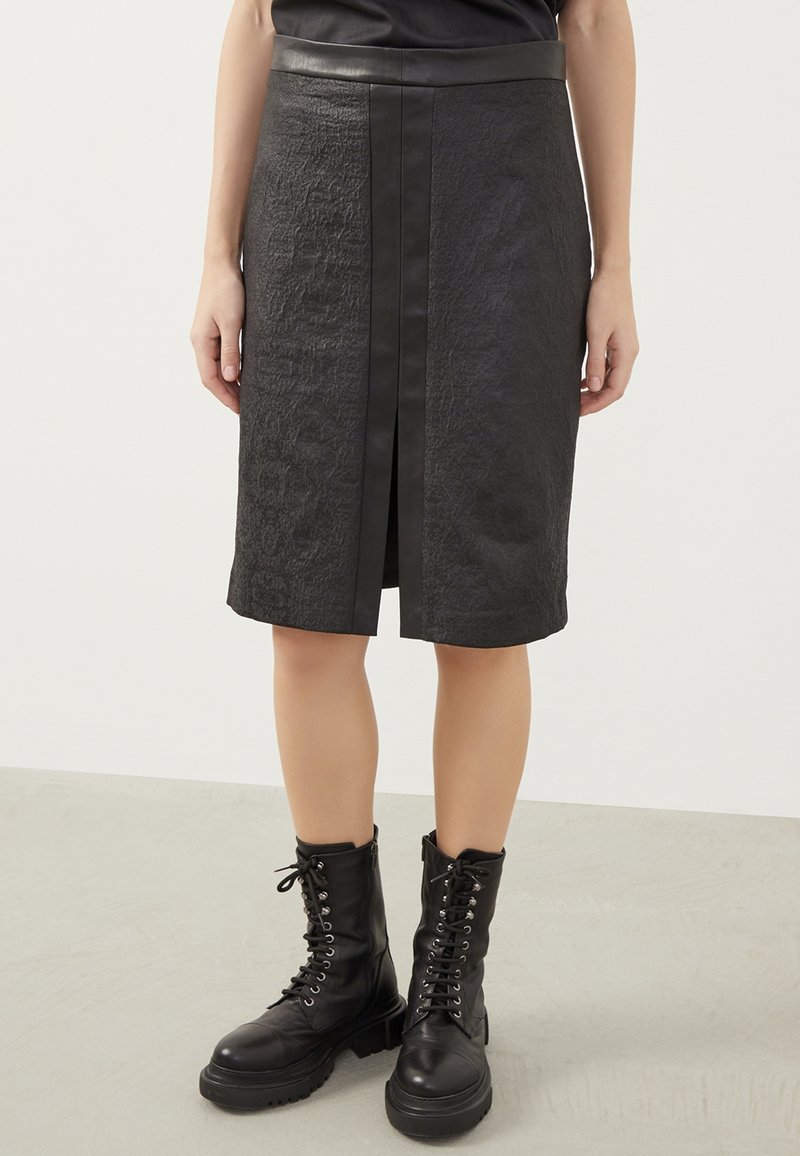 Zwarte leren rok met een gestructureerde afwerking, midi-lengte, voorzien van een voorkeursploit en een soepele tailleband, gecombineerd met zwarte veterlaarzen.