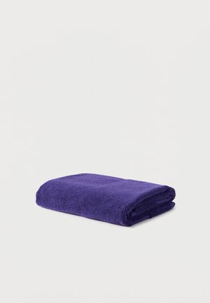 Serviette violet profond pliée sur une surface blanche, montrant un tissu doux au toucher et des bords soignés.