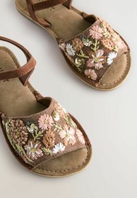 Sandali marroni con ricami floreali in rosa, bianco e oro. Materiale in suede morbido, design open toe e cinturini regolabili.
