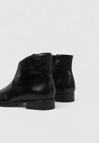 Botines de cuero negro con una textura suave, puntera redondeada y un tacón de bloque bajo. Cuenta con una cremallera lateral funcional para facilitar su uso.
