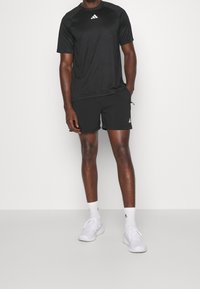 Svart idrottströja och shorts, båda i lättviktstyg. T-shirten har en liten vit logotyp på bröstet. Vita sneakers och strumpor.