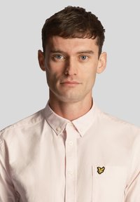 Camicia collared rosa chiaro con bottoni sul davanti, caratterizzata da un tessuto testurizzato e un piccolo logo ricamato di una farfalla gialla sul taschino sinistro.