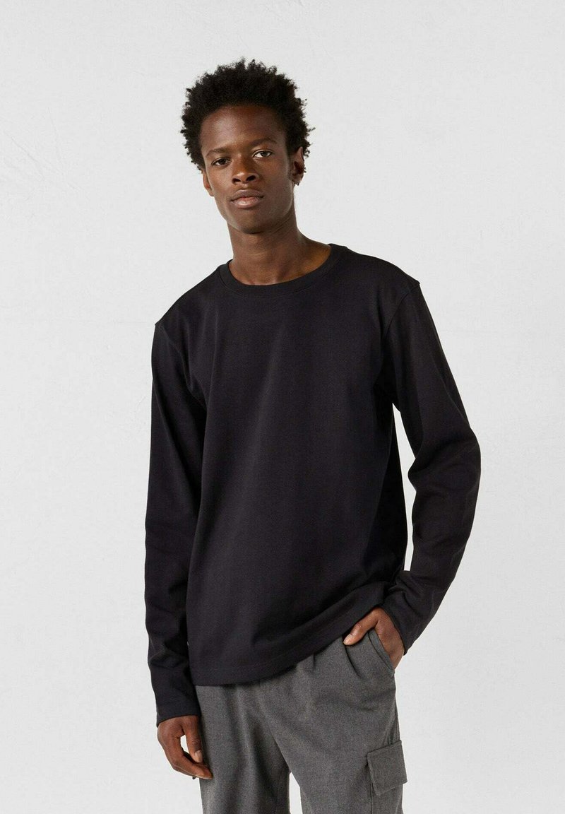 Maglietta nera a maniche lunghe in cotone con collo a giro, vestibilità rilassata e superficie leggermente tessuta, abbinata a pantaloni cargo grigi.