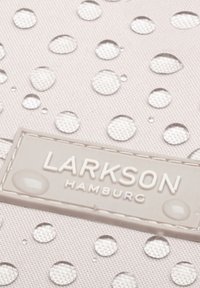 Világosszürke szövet, emelt vízcseppekkel, amelyen egy téglalap alakú, texturált címke látható, a "LARKSON HAMBURG" felirattal, világosabb árnyalatban.