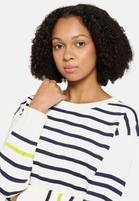 Sweter w marynarskie paski w kolorze granatowym i białym o luźnym kroju. Posiada zielone akcenty na mankietach, miękki materiał oraz szeroki dekolt.