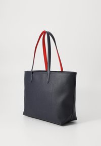Sac en cuir texturé bleu marine avec des anses rouges, de forme rectangulaire et une poche avant. Fini lisse avec des accents contrastés.