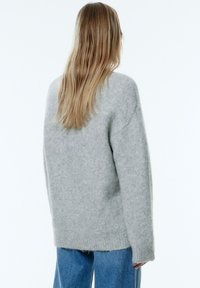 Grijze gebreide trui gemaakt van zachte stof, met een losse pasvorm, lange mouwen en geribbelde manchetten, gecombineerd met blauwe jeans.