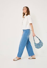 Weißes, kurzärmliges Hemd mit Knopfleiste; hellblaue, lockere Jeans; beige Rutschen-Sandalen; strukturierte blaue Handtasche mit Diamant-Muster.