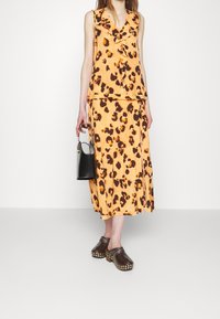 Haut sans manches à imprimé léopard orange associé à une jupe assortie. Accessoire : petit sac à main noir. Chaussures : sabots marron foncé avec des clous.