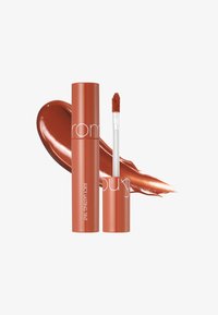 Lápiz labial líquido en un tubo naranja con texto blanco. Incluye un aplicador en forma de pie de ciervo y una muestra del mismo tono en el fondo.