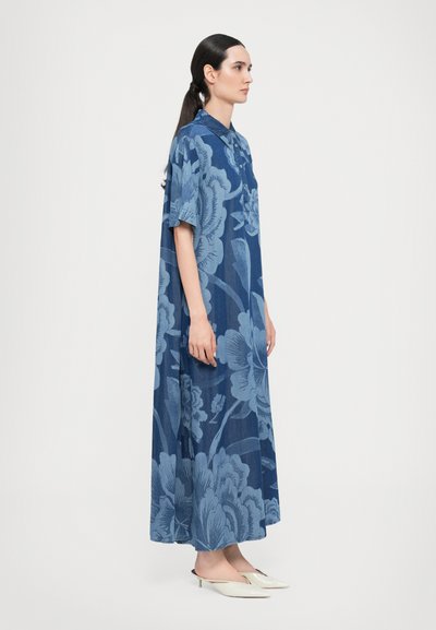 Rochie cu imprimeu floral albastru, cu mâneci scurte, guler și o croială lejeră. Țesătură texturată și o siluetă lungă. Papuci minimalisti purtați.