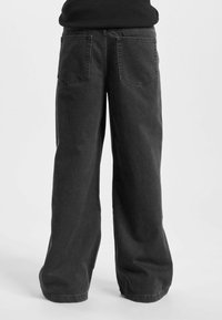 Jeans de denim negro de pierna ancha con un ajuste relajado, que cuentan con dos bolsillos traseros y detalles de costura visibles, acabado de tela texturizada.
