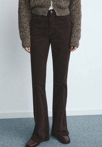 Bruine corduroy flared broek met een gladde textuur. Voorzien van steekzakken aan de voorkant en een hoge taille. Draagt een gebreide, kortere trui erbij.