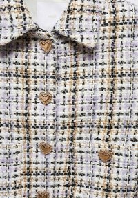 Veste tissée à motifs avec des fils beige, noirs et violets, avec un col et quatre boutons en forme de cœur dorés sur le devant.
