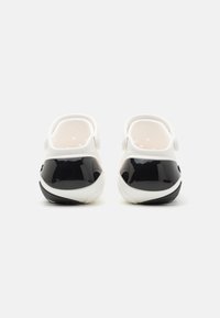 Black and white clogs with a glossy black finish on the back and a white perforated upper. Soft texture and rounded shape.
