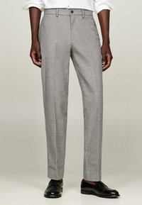 Pantaloni grigi su misura con un tessuto a trama, caratterizzati da un taglio dritto, pince davanti e chiusura con bottone. Scarpe eleganti nere.