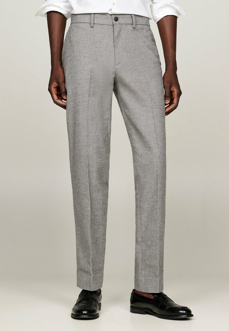 Pantaloni grigi su misura con un tessuto a trama, caratterizzati da un taglio dritto, pince davanti e chiusura con bottone. Scarpe eleganti nere.